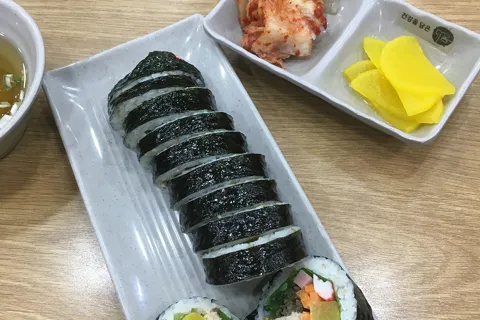 A sliced gimbap roll with kimchi and yellow pickled radish on a white plate