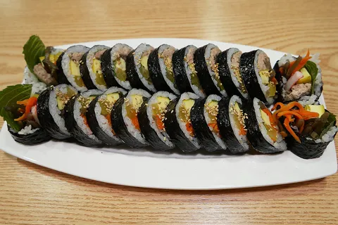 Sliced gimbap with carrot, pickled radish and perilla leaves on an oval white plate