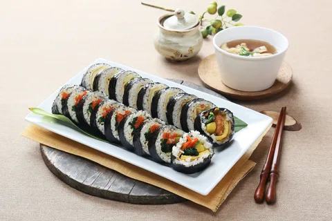 Gimbap slices on a white dish beside a bowl of egg soup and chopsticks